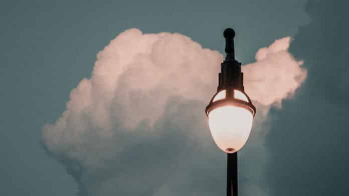 A streetlight against some fluffy white clouds.