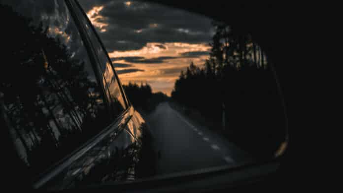 A bleak sunset in the rear view mirror of a black car.